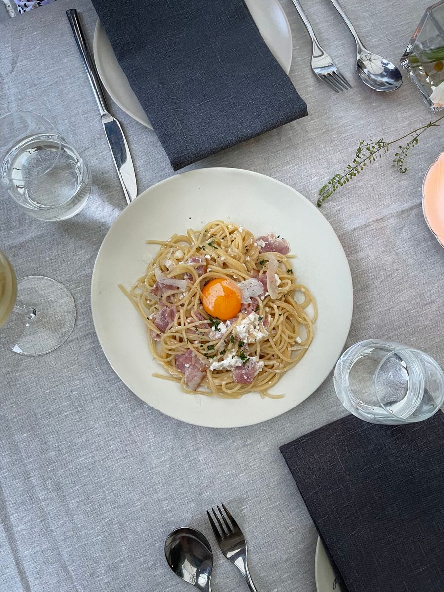 Um prato de spaghetti alla carbonara com gema de ovo por cima, numa mesa posta