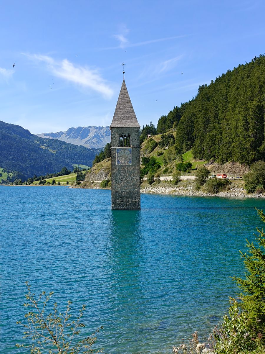 A torre do sino que sai das águas do Lago di Resia, com montanhas atrás