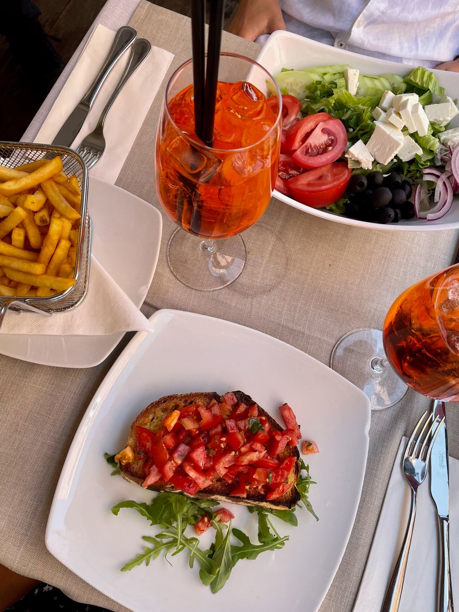 Um spritz, bruschetta e salada numa mesa ao ar livre