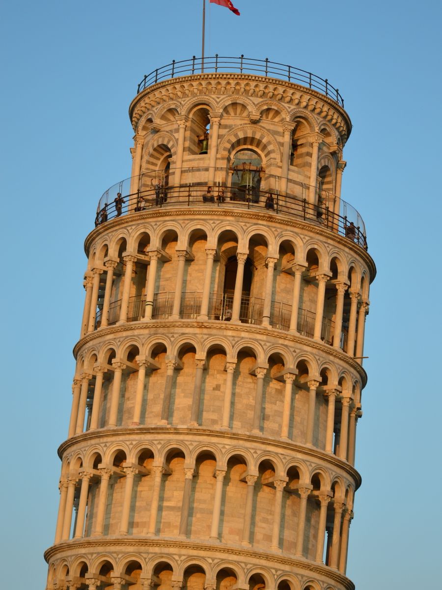 O alto da Torre de Pisa contra o céu azul, com visitantes no topo