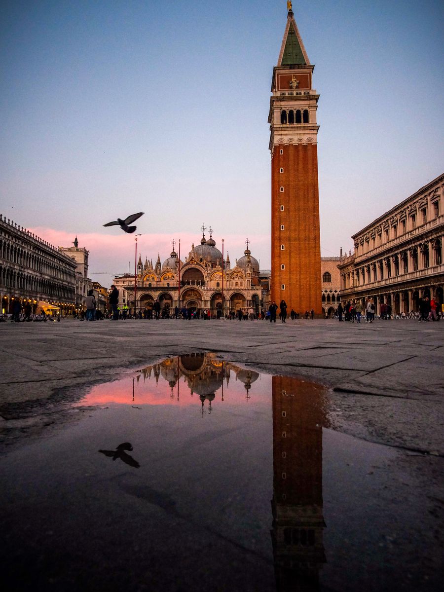 A Piazza San Marco e o campanário refletidos numa poça ao entardecer