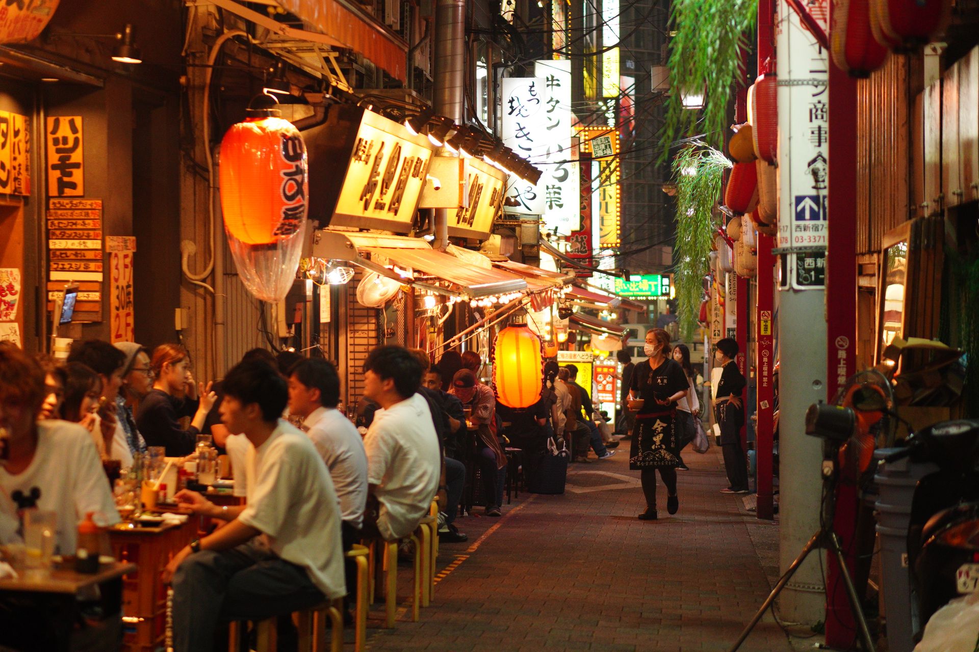 Pessoas jantam num beco estreito de Shinjuku iluminado por lanternas de papel