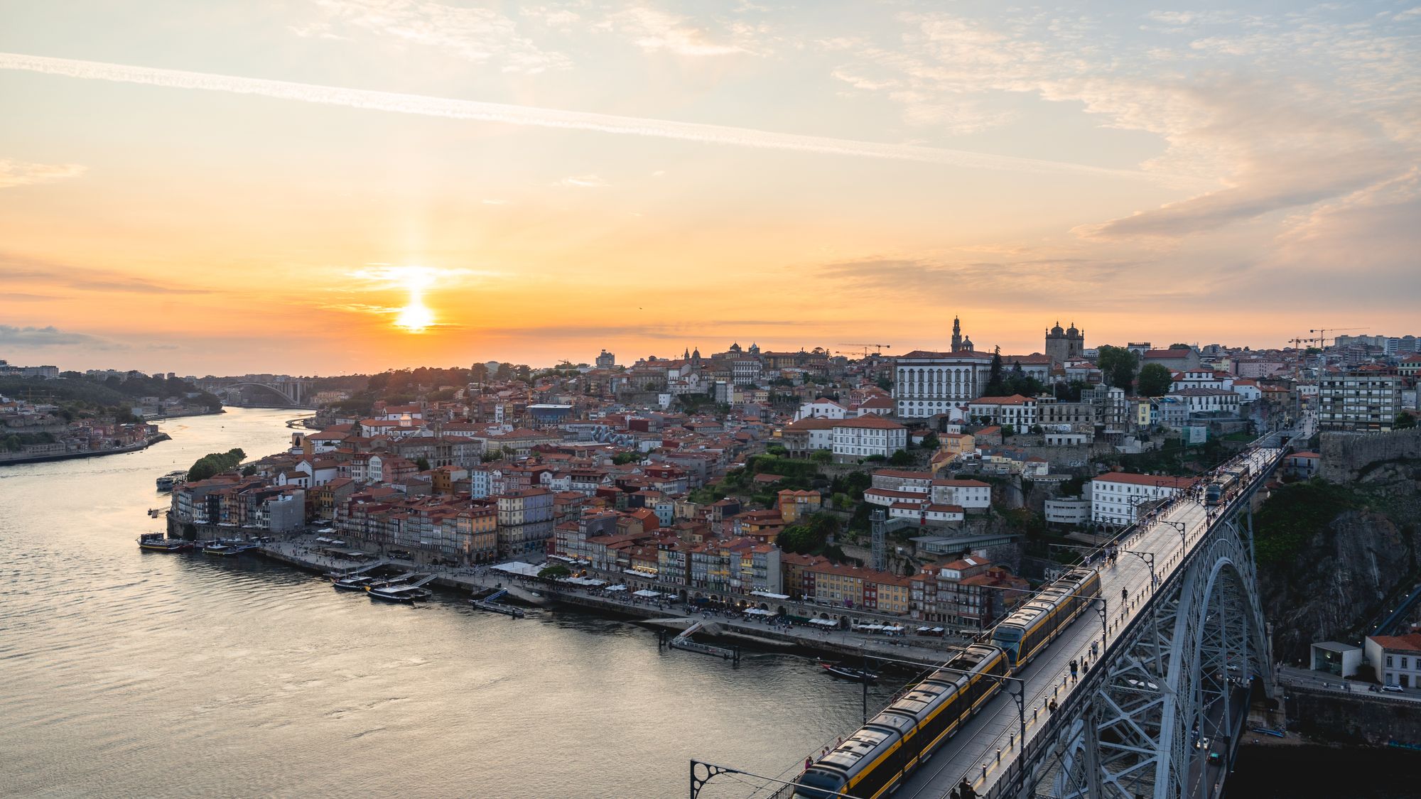 Pôr do sol sobre o Douro, no Porto, com a Ponte Luís I e o metrô atravessando o tabuleiro de cima
