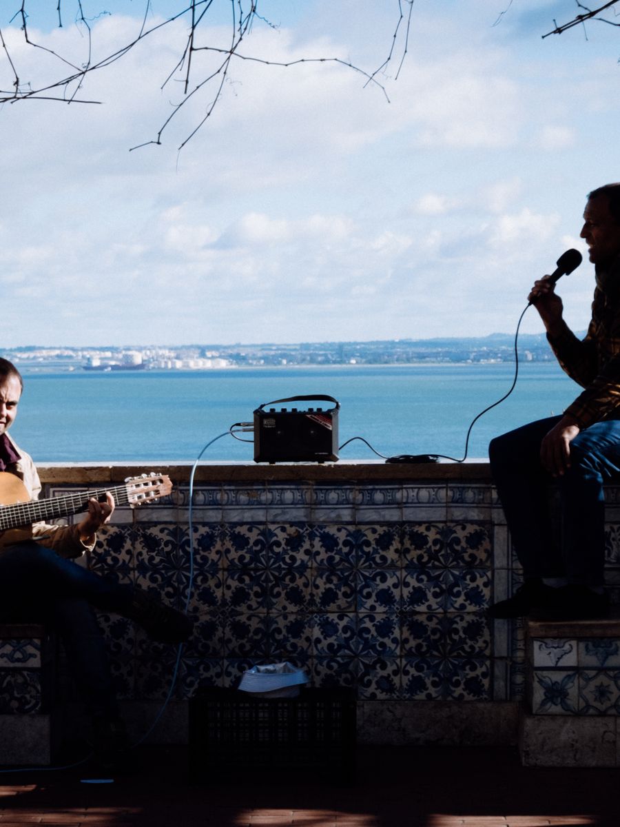 Dois músicos tocando num miradouro de Lisboa, com o Tejo ao fundo