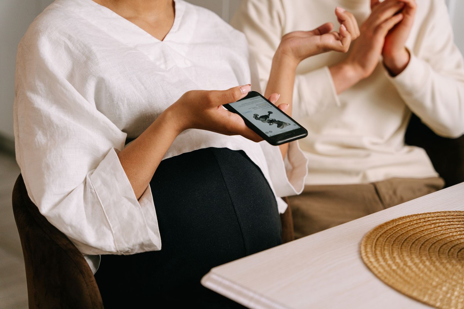 Gestante sentada à mesa, mostrando no celular a imagem de um ultrassom